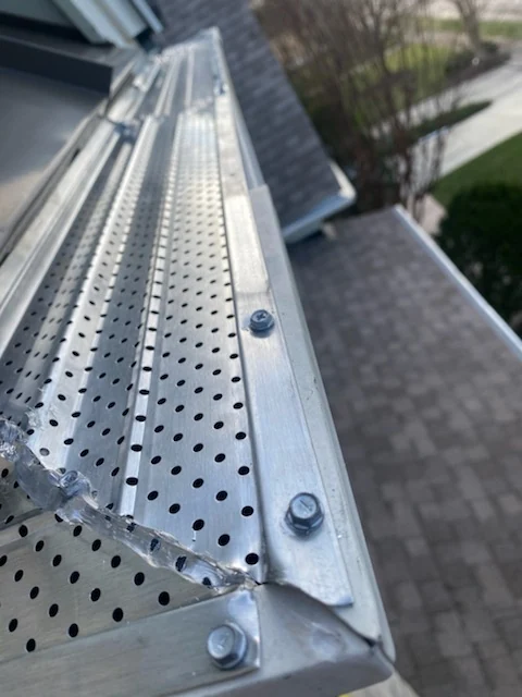 Newly fitted perforated aluminium gutter guard screwed down at a corner joint